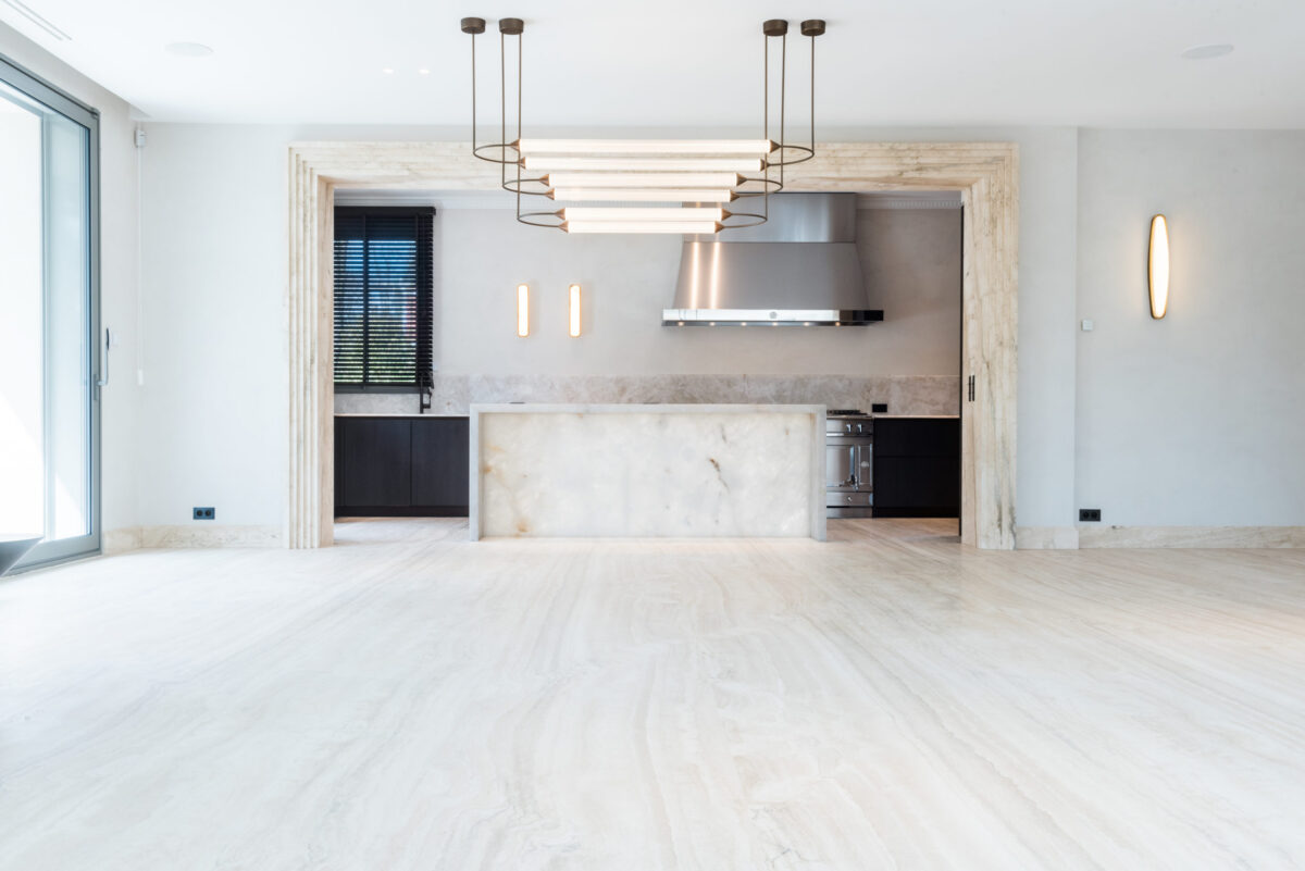Séjour ouvert sur une cuisine, sol en travertin clair veiné, îlot en quartzite blanche translucide et encadrement en pierre