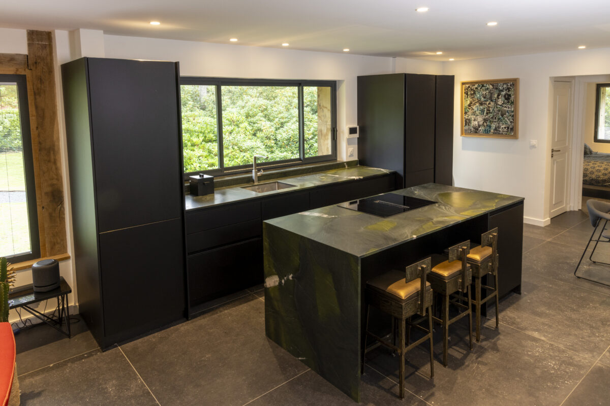 Cuisine aux façades noires avec îlot en quartzite vert veiné et tabourets de bar