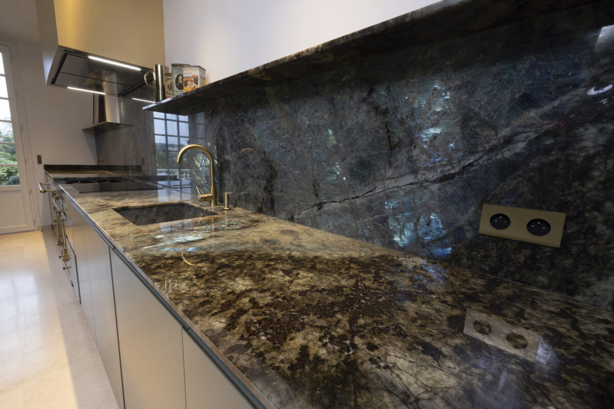 Robinet noir sur un plan de cuisine et une crédence en labradorite bleue irisée