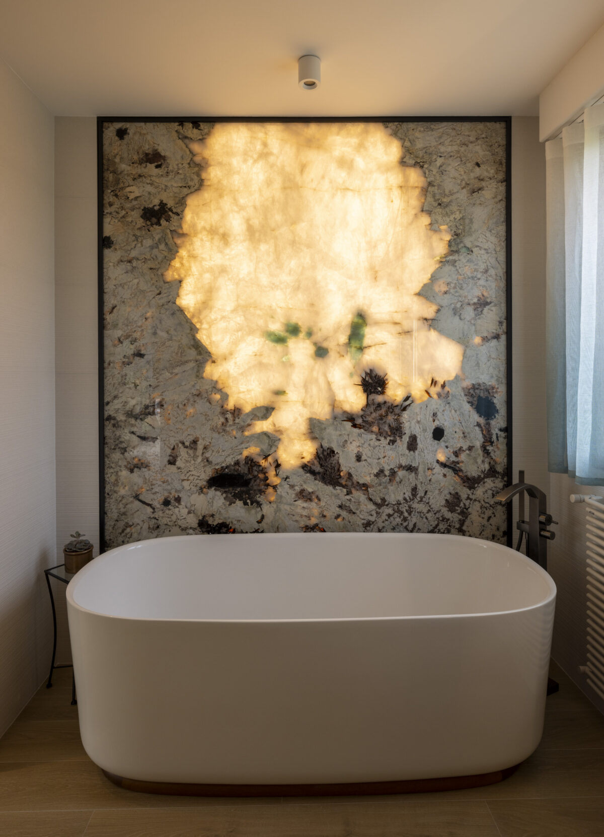 Salle de bain avec baignoire îlot devant un mur en pierre translucide rétroéclairée