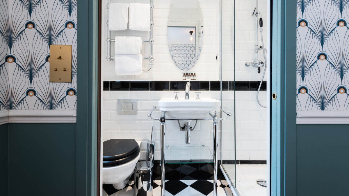 Petite salle de bain parisienne en faïence métro blanche avec frise noire, papier peint Art déco et sol en damier noir et blanc
