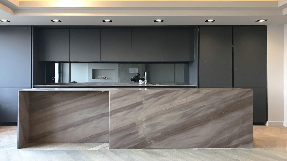 Îlot de cuisine en quartzite brun chaud veiné entre des façades sombres