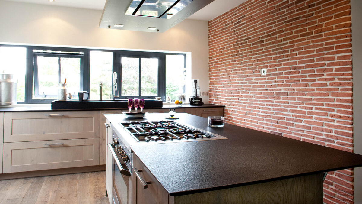 Îlot de cuisine avec plan de travail en granit noir finition cuir devant un mur de briques