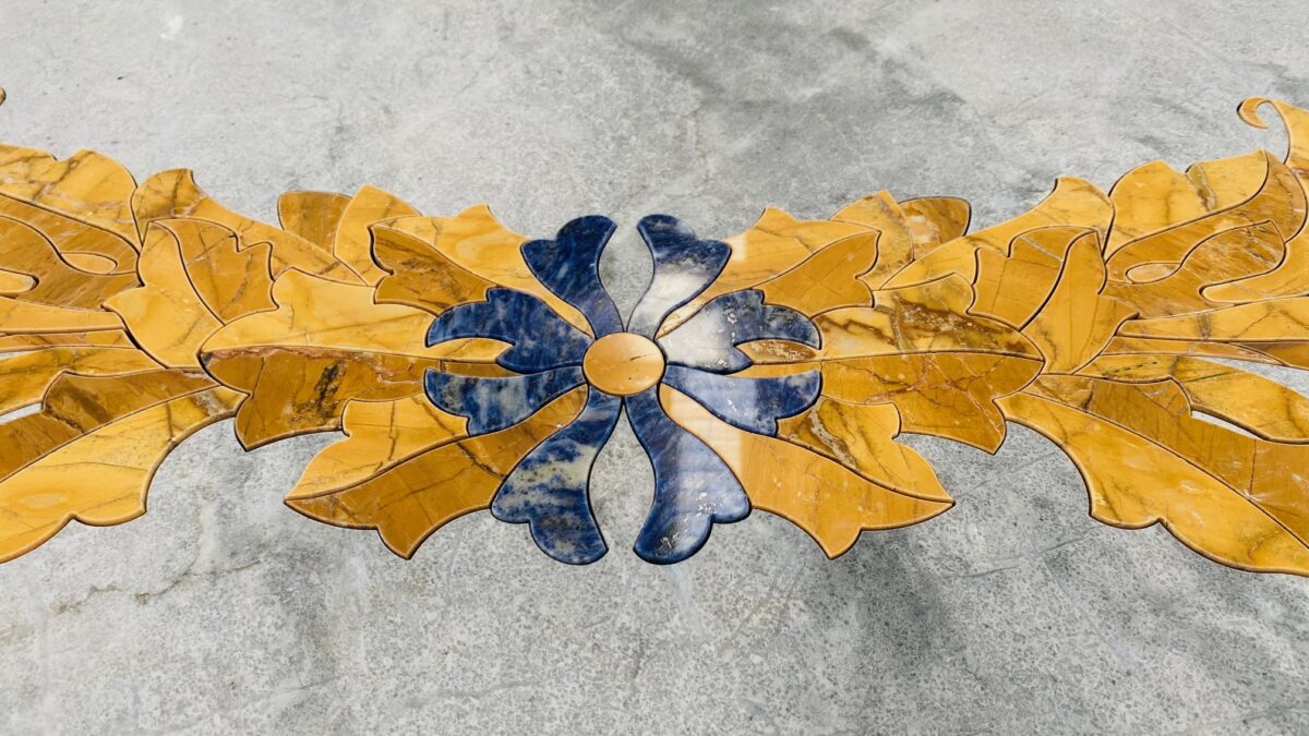 Marqueterie de marbres, feuilles jaunes et fleur bleue en cours de pose sur une dalle grise