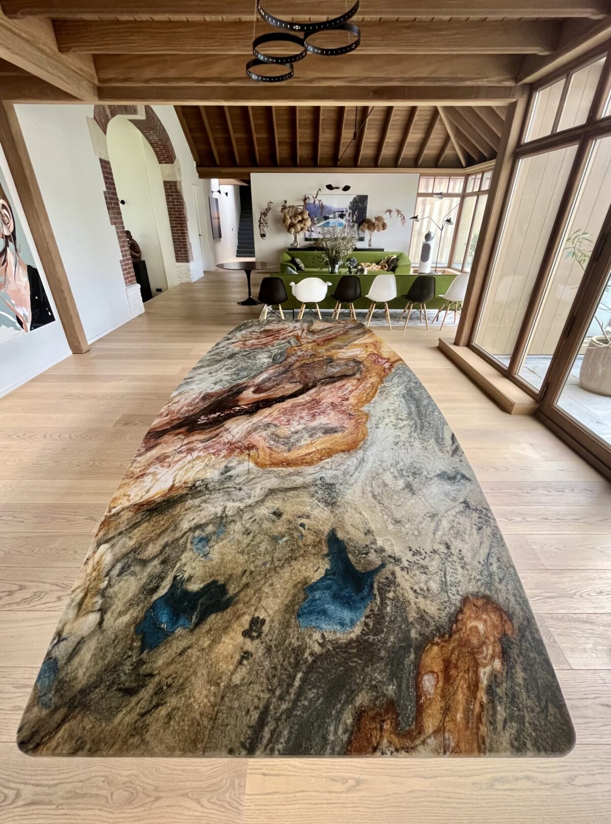 Longue table en quartzite Colibri Blue aux veines bleues et cuivrées dans un séjour à charpente apparente