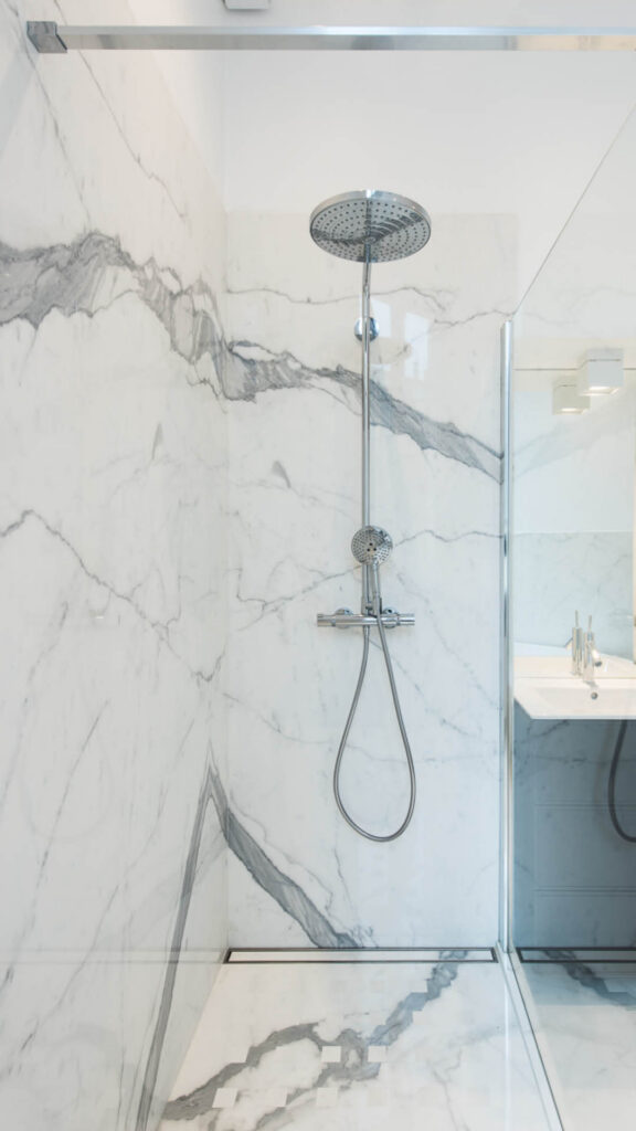 Pommeau de douche fixé sur un mur en marbre blanc et gris veiné