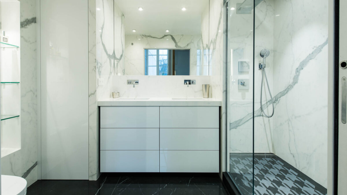 Salle de bain habillée de marbre blanc aux veines grises, meuble vasque blanc et douche vitrée