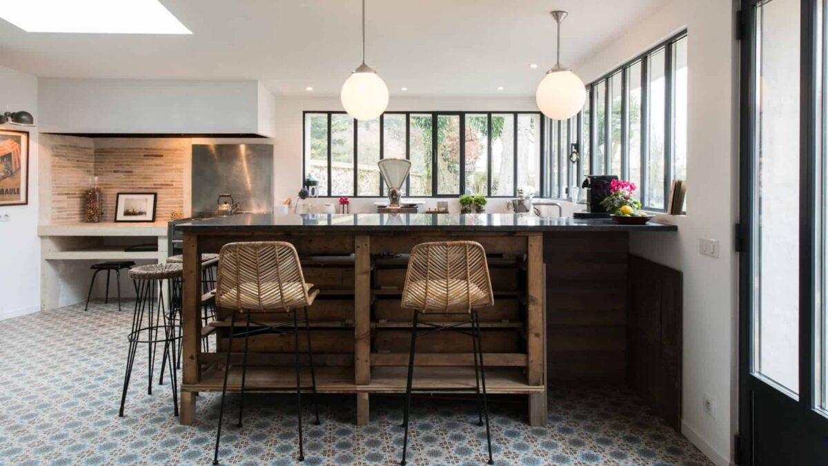 Cuisine avec îlot en bois et plan de travail en pierre bleue belge, tabourets en rotin devant une verrière