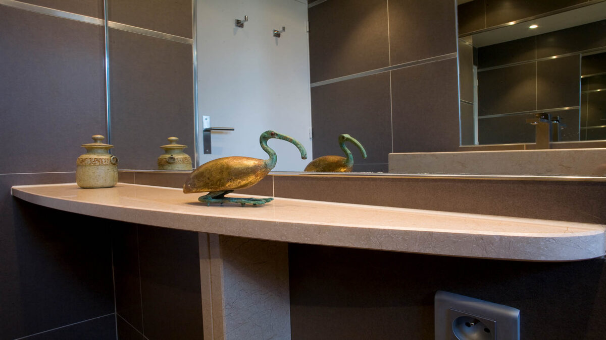 Tablette plan vasque en pierre beige sur carrelage anthracite avec mitigeur dans le miroir