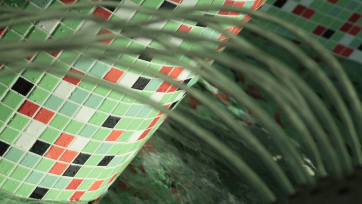 Mosaïque de piscine aux tesselles vertes, rouges et noires sous un jet d'eau