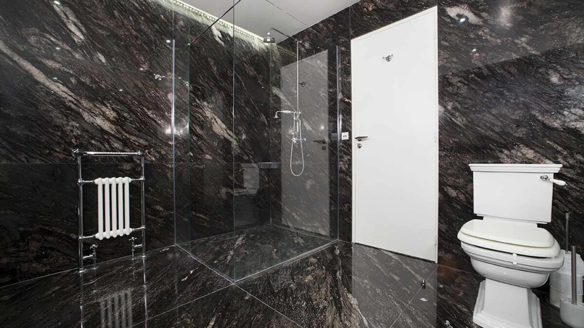 Douche à l'italienne habillée de granit noir veiné avec porte vitrée et radiateur sèche-serviettes