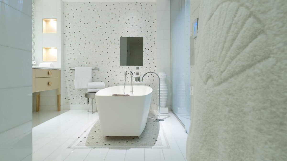 Salle de bains d'hôtel avec baignoire îlot et mur en mosaïque blanche à touches sombres