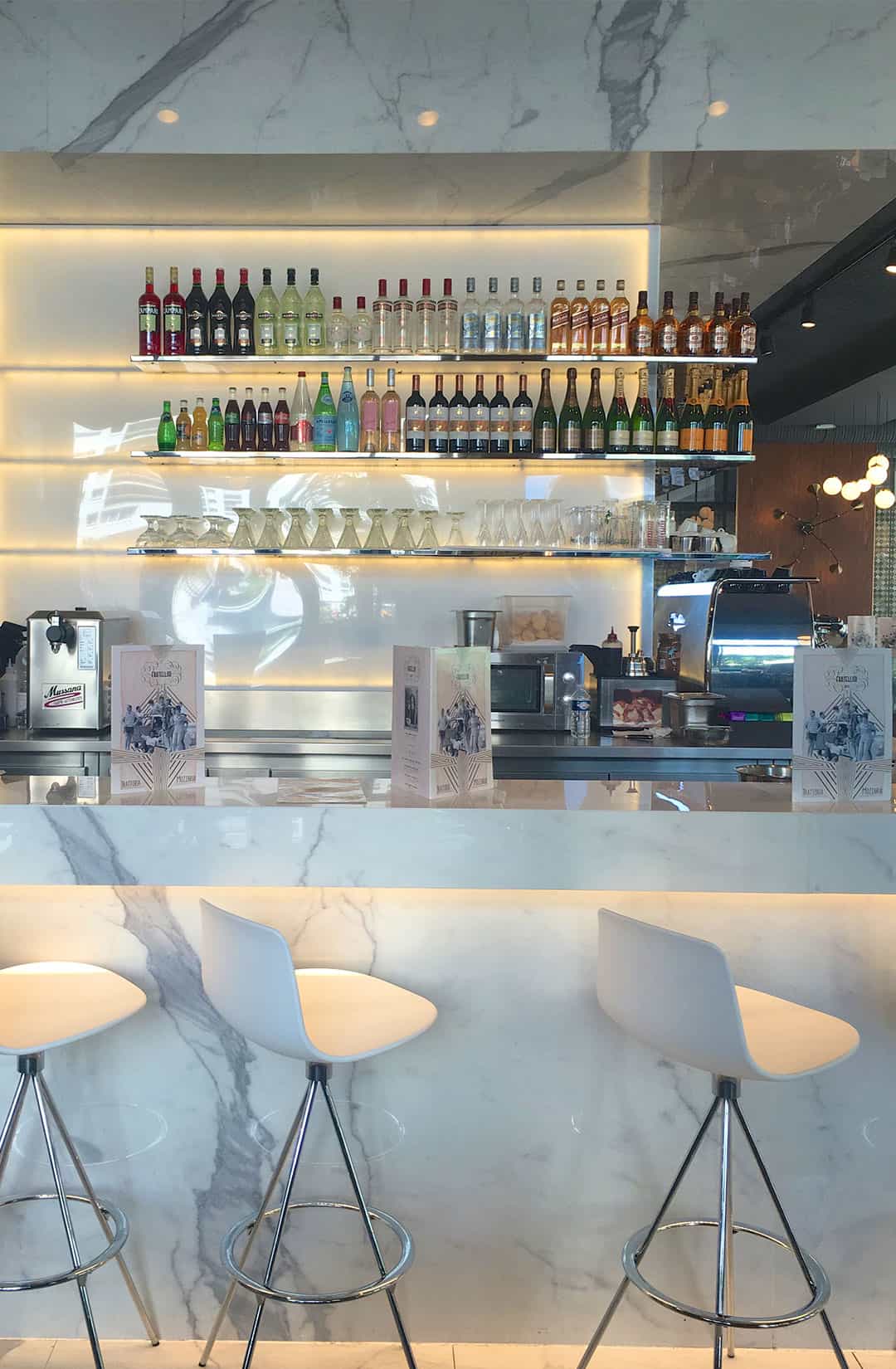 Comptoir de bar en marbre Calacatta avec tabourets blancs et étagères de bouteilles rétroéclairées