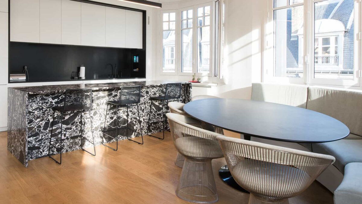 Cuisine ouverte avec plan de travail et crédence en marbre veiné noir sous une verrière