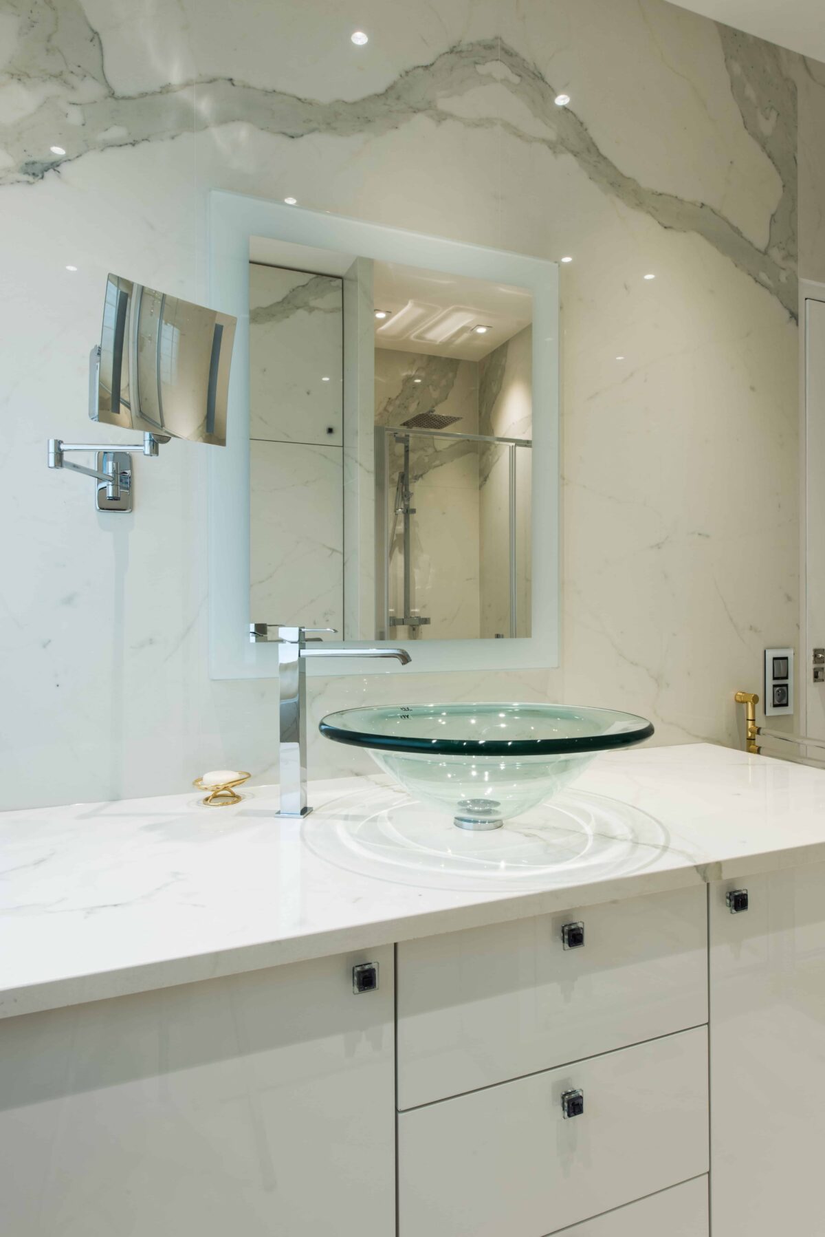 Salle de bain en céramique effet marbre statuaire blanc veiné de gris, vasque en verre posée sur un plan blanc sous un miroir