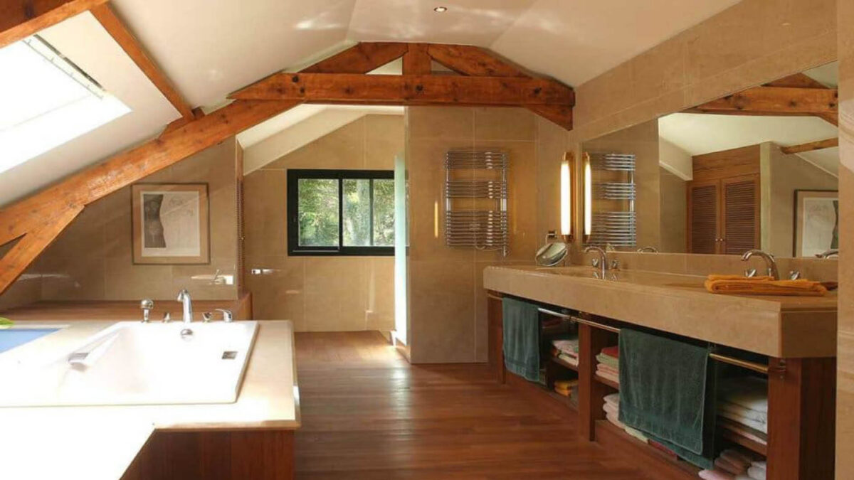Salle de bains sous combles avec baignoire et plan vasque en pierre beige, sèche-serviettes