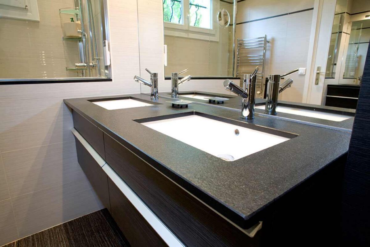 Plan double vasque en granit noir sur meuble en bois sombre avec mitigeurs chromés