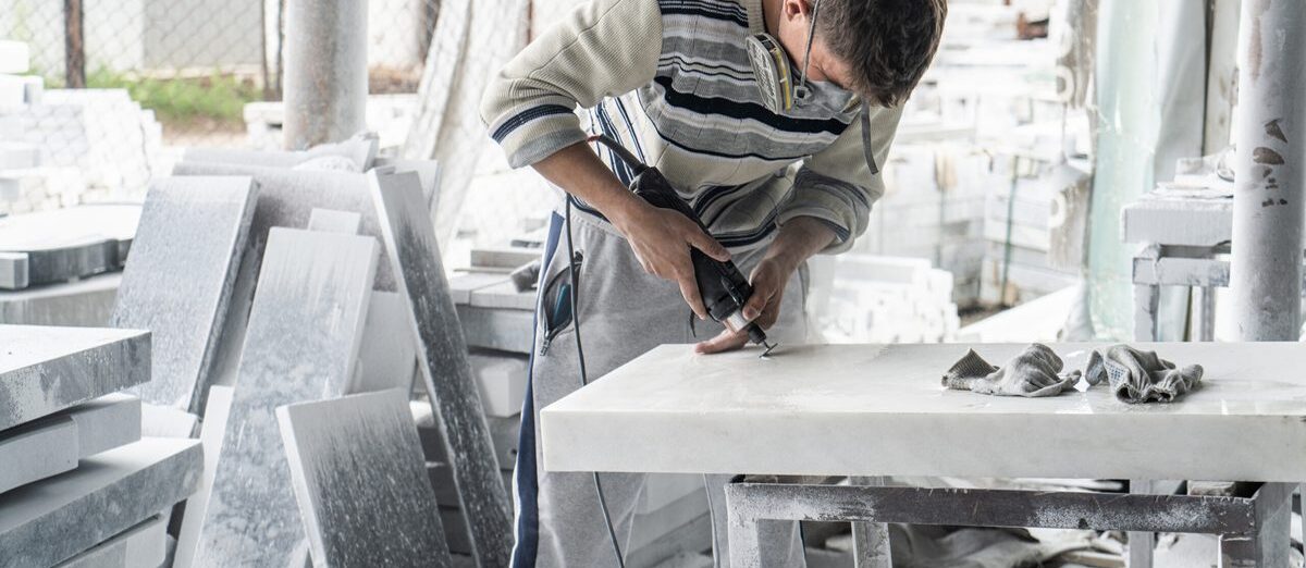 Marbrier à l’atelier, ponceuse à la main, sur un plan en marbre blanc