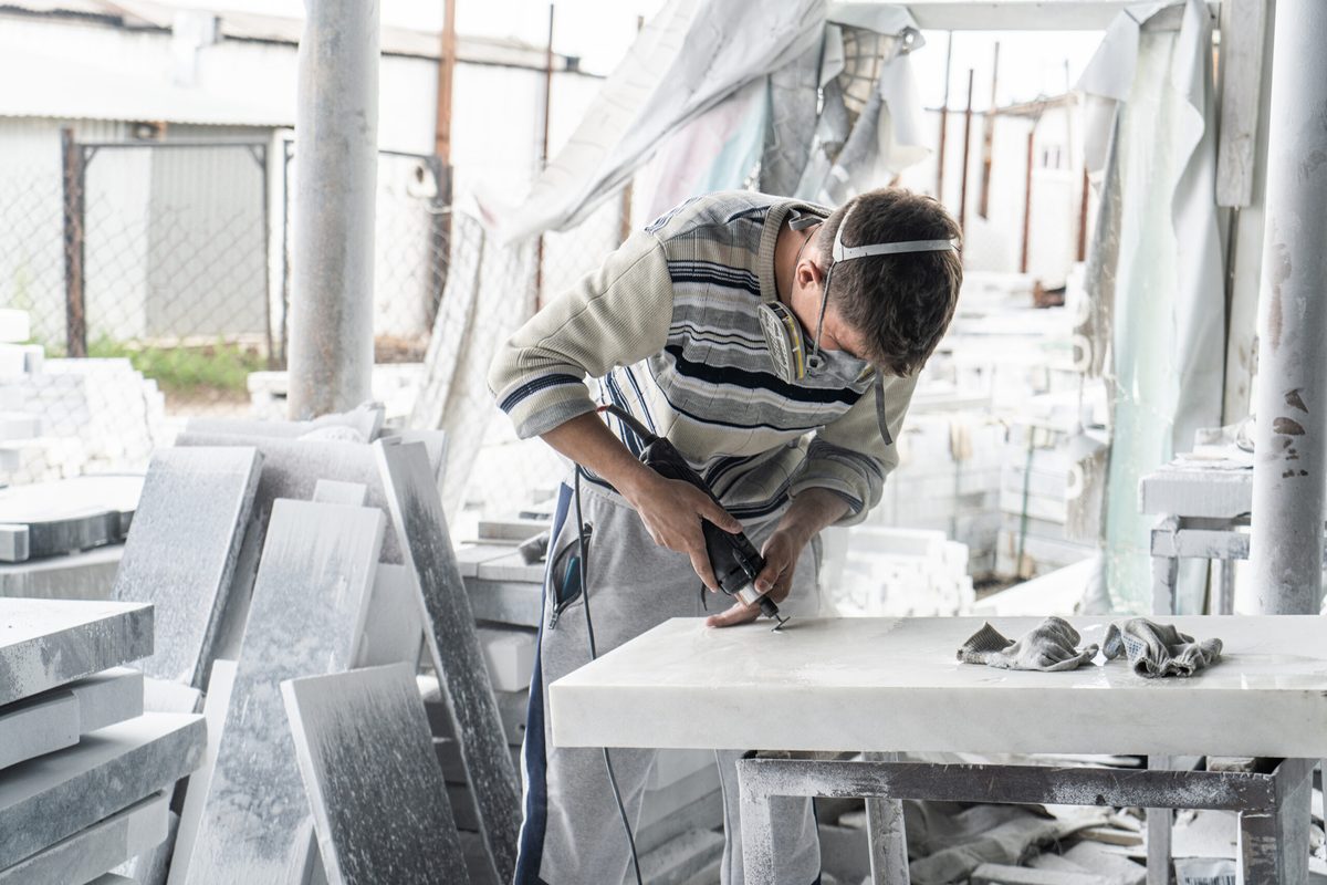 Marbrier à l’atelier, ponceuse à la main, sur un plan en marbre blanc