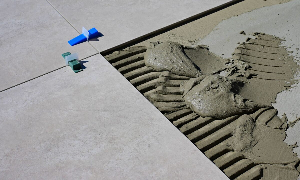 Application au peigne cranté d'un mortier de pose sur un carrelage gris grand format, avec des cales de joint