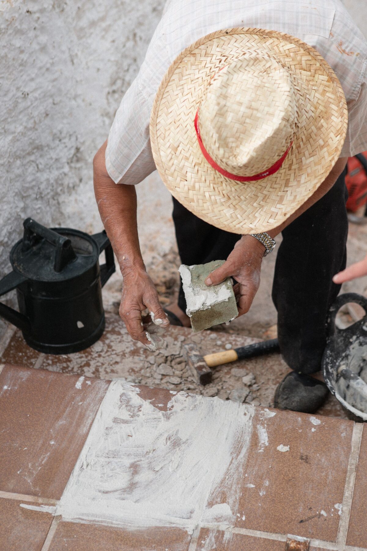 Artisan au chapeau de paille étalant du mortier à la truelle sur un carreau posé au sol