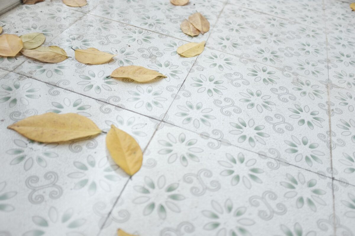 Carreaux de ciment beige à motif floral discret jonchés de quelques feuilles