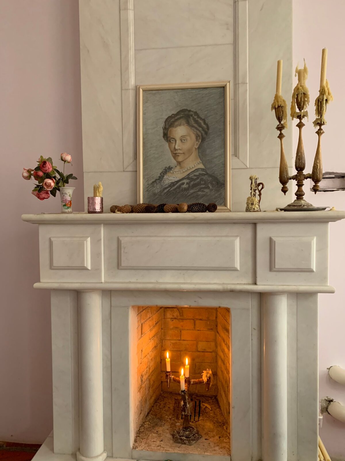 Cheminée ancienne en marbre clair avec tableau et chandeliers sur la tablette, feu allumé
