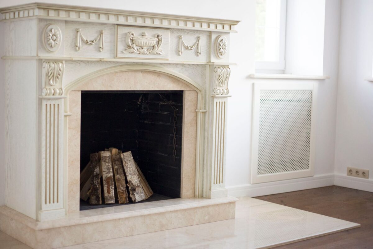 Cheminée classique en marbre blanc à linteau sculpté de guirlandes, bûches dans le foyer