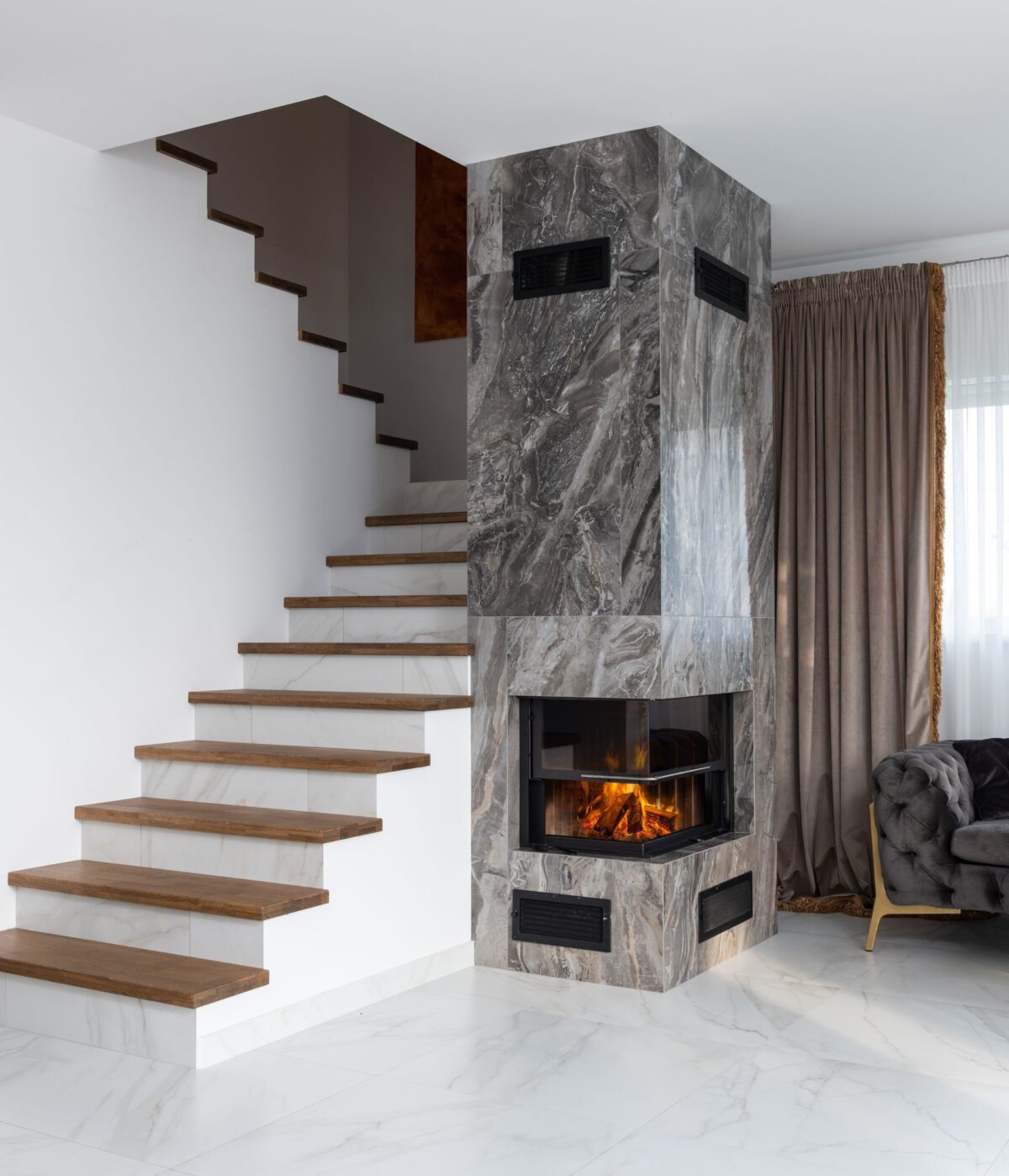 Cheminée habillée de marbre gris au pied d'un escalier en bois