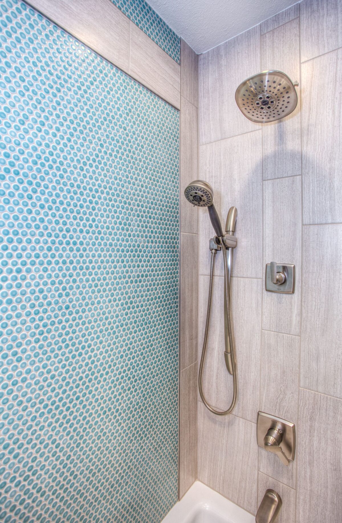 Douche avec mur en mosaïque de faïence bleu turquoise et eau ruisselante sur les carreaux, pommeau chromé