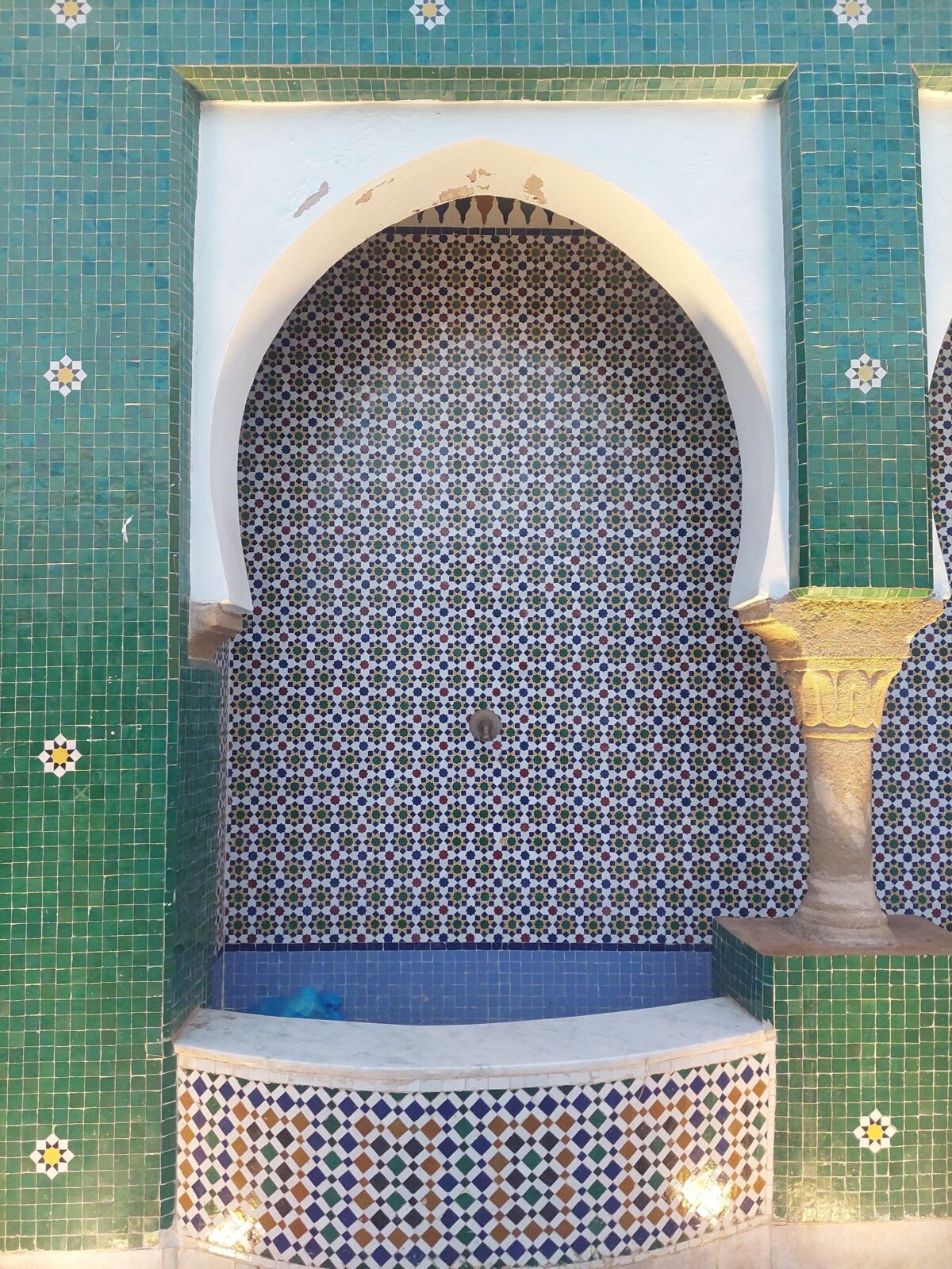 Fontaine murale en mosaïque verte et blanche encadrée d'une arche marocaine