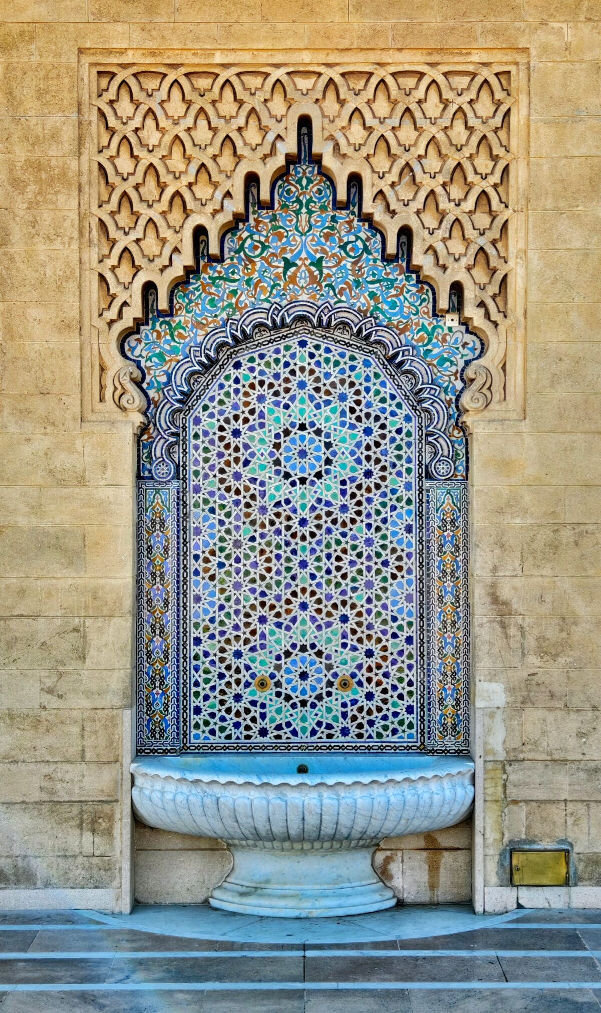 Fontaine murale marocaine richement décorée de mosaïques bleues et ocres sous une arche en étoile