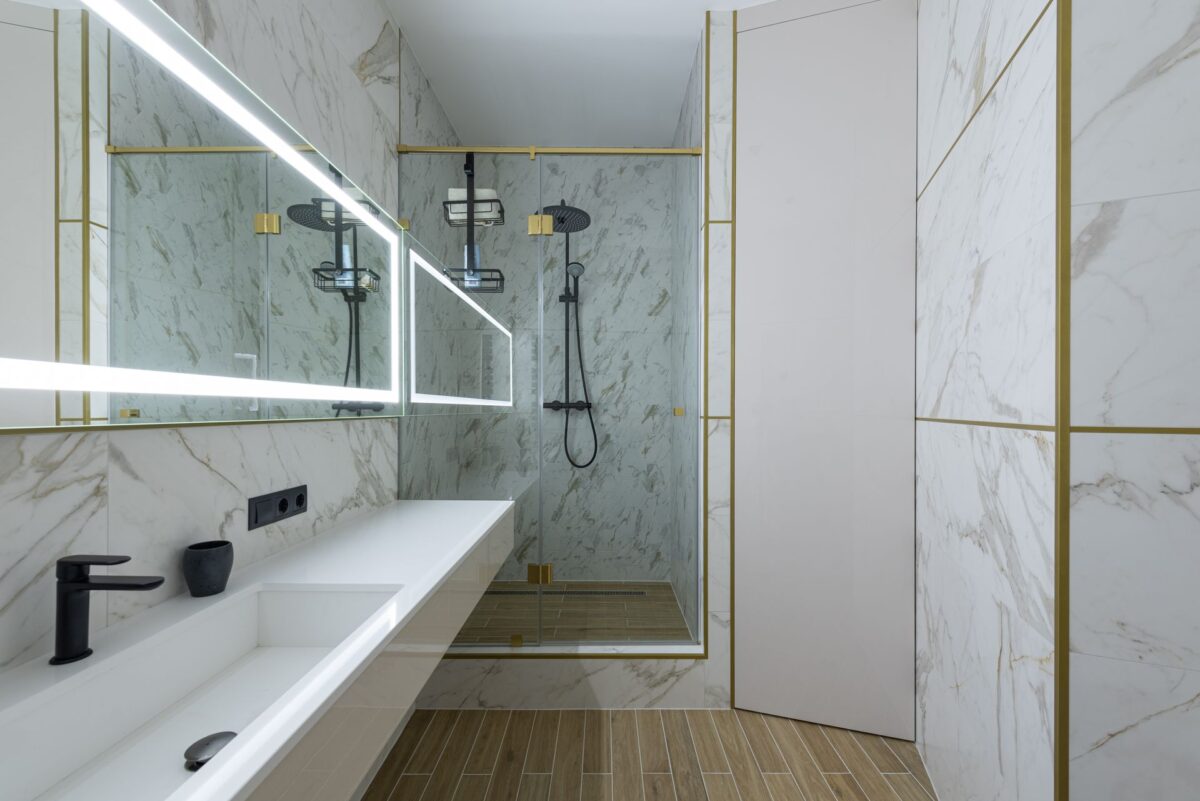 Salle de bain en grandes dalles aspect marbre avec profilés dorés et douche à l'italienne