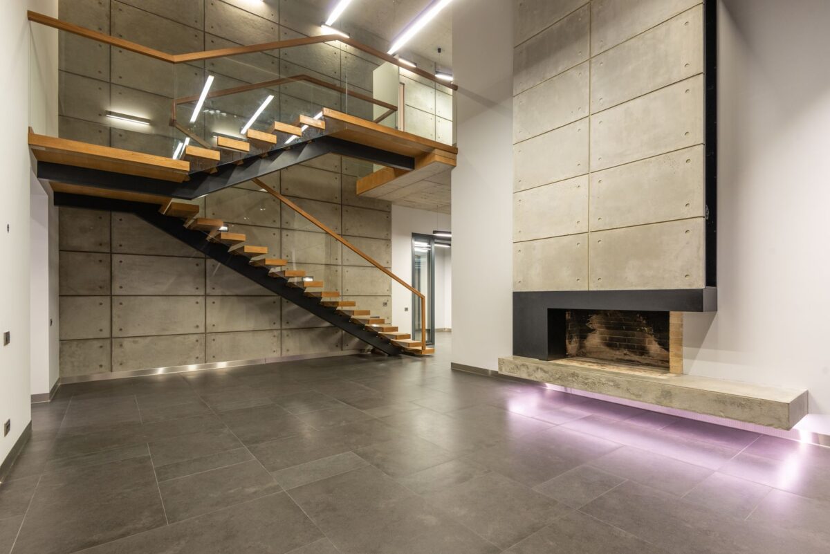 Intérieur épuré avec cheminée et escalier ajouré sur un sol gris grand format