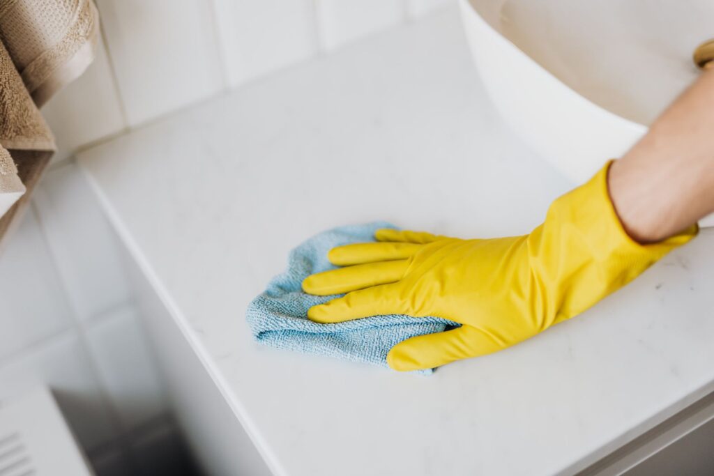 Main gantée de jaune essuyant un plan en marbre blanc avec un chiffon bleu