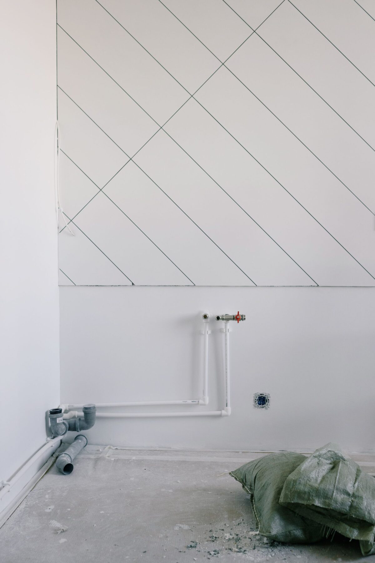 Mur de carreaux de faïence blancs posés en chevron, chantier de rénovation avec tuyauterie apparente au sol