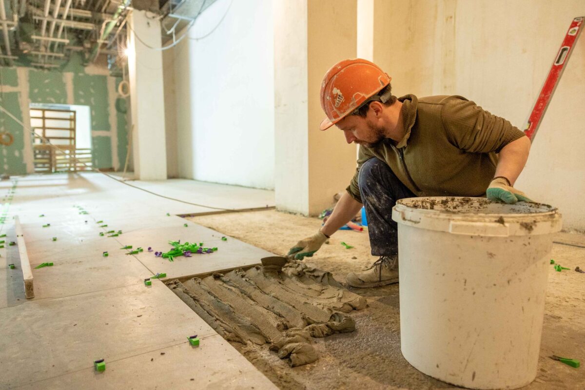 Ouvrier en tenue de chantier qui pose un mortier au sol lors d'une rénovation intérieure