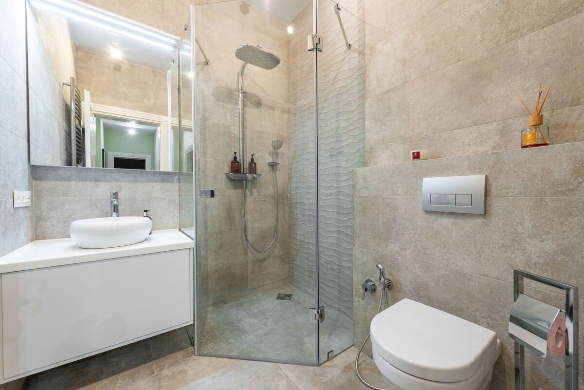 Salle de bain avec paroi de douche en verre, carrelage beige et meuble vasque blanc