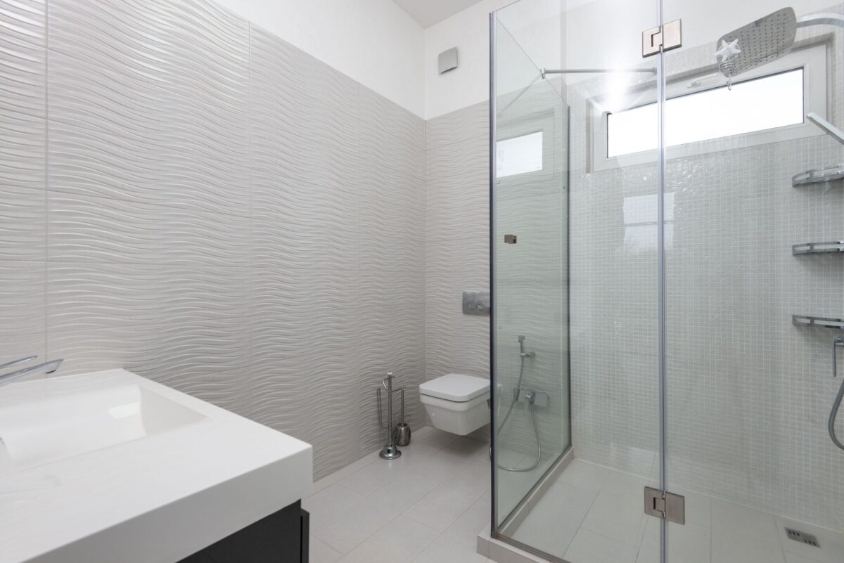Douche à paroi de verre fixe dans une salle de bain blanche aux murs texturés