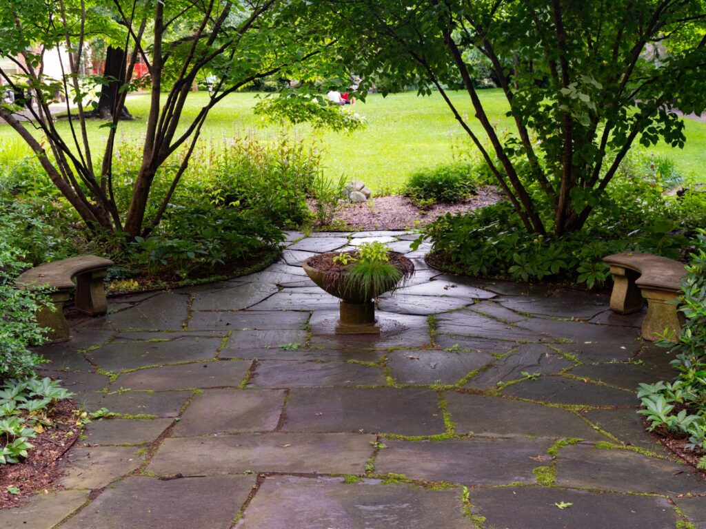 Patio en dalles de pierre sombre entouré de verdure dans un jardin