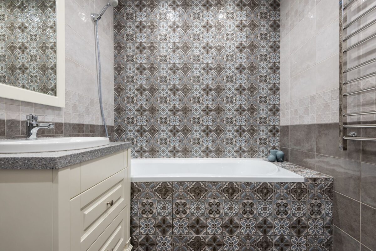 Salle de bain avec baignoire habillée de carreaux de ciment à motifs gris et meuble vasque blanc