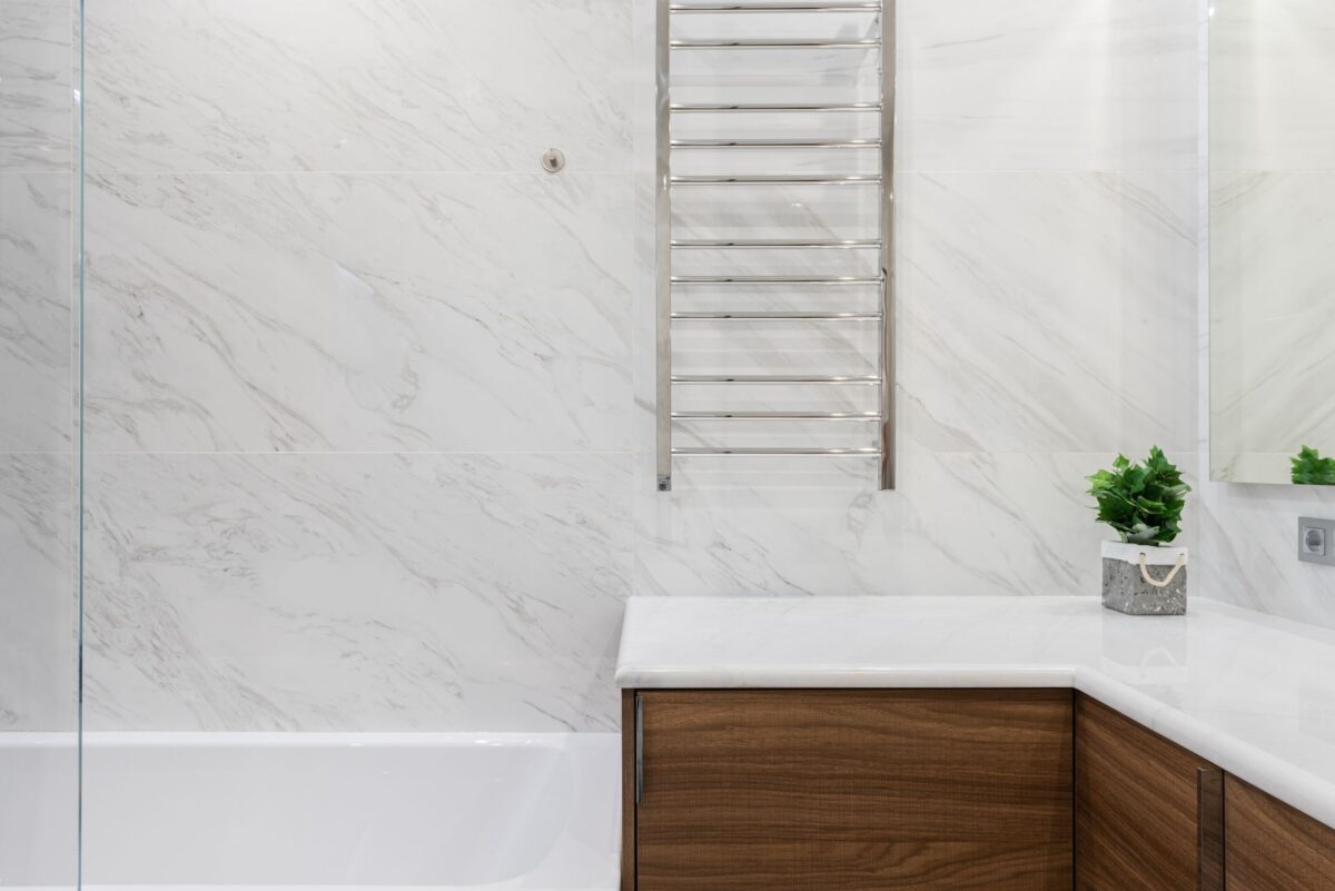Salle de bain en carrelage effet marbre blanc veiné avec un meuble vasque en bois clair et des plantes