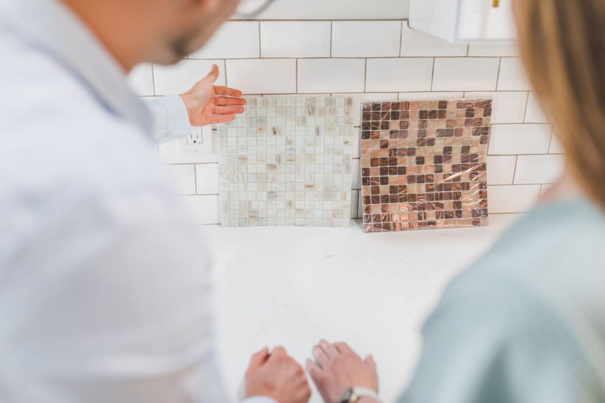Un professionnel présente des carreaux à des clients près d'un mur carrelé de cuisine