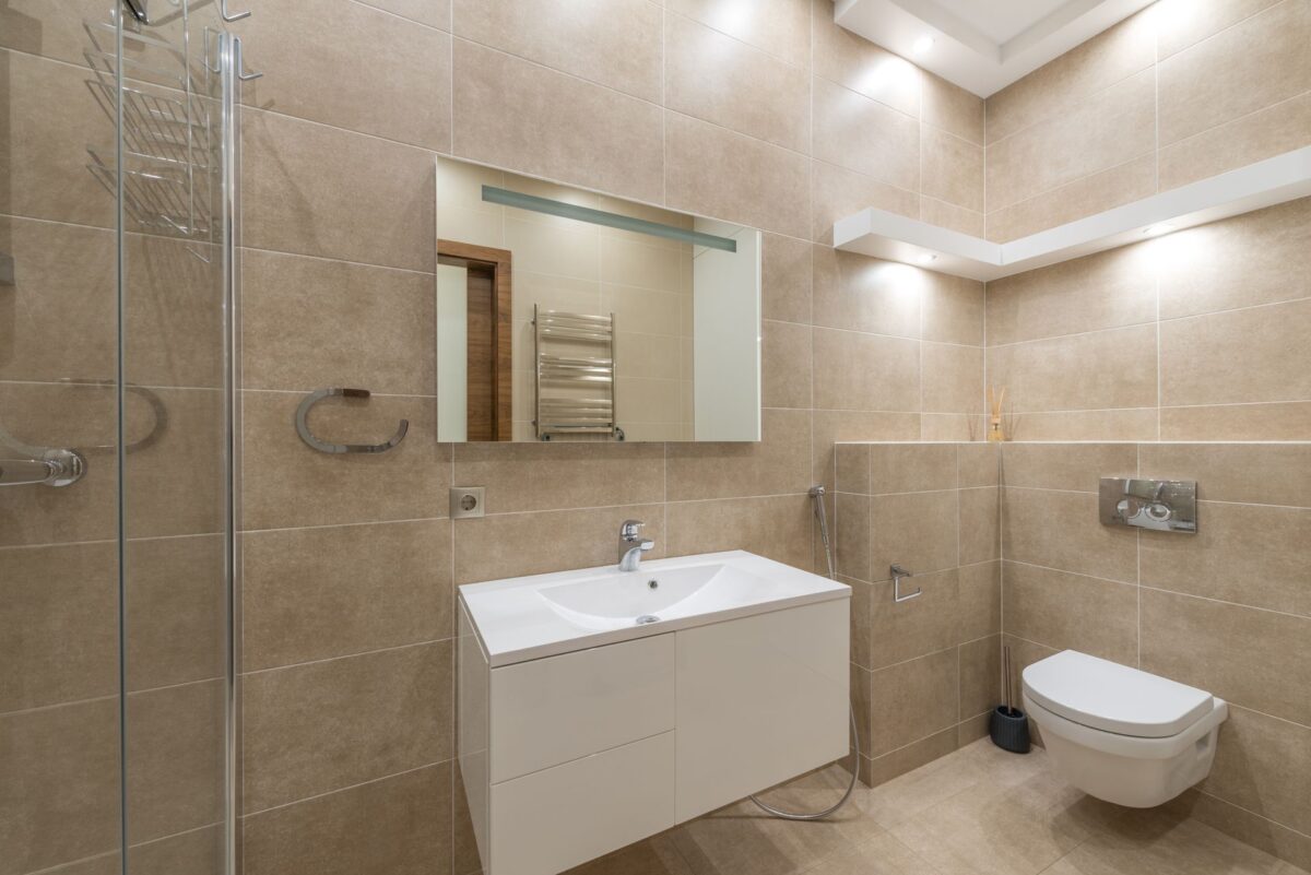 Salle de bain beige avec WC suspendu, meuble vasque blanc et grand miroir
