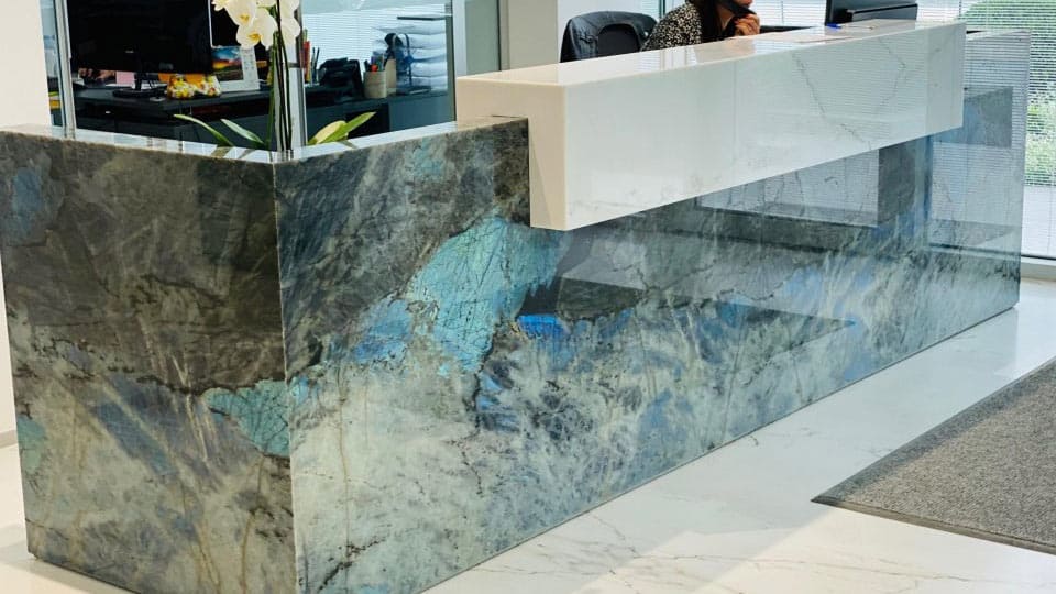 Banque d'accueil habillée de labradorite aux reflets bleus, plateau blanc, dans un espace de bureaux