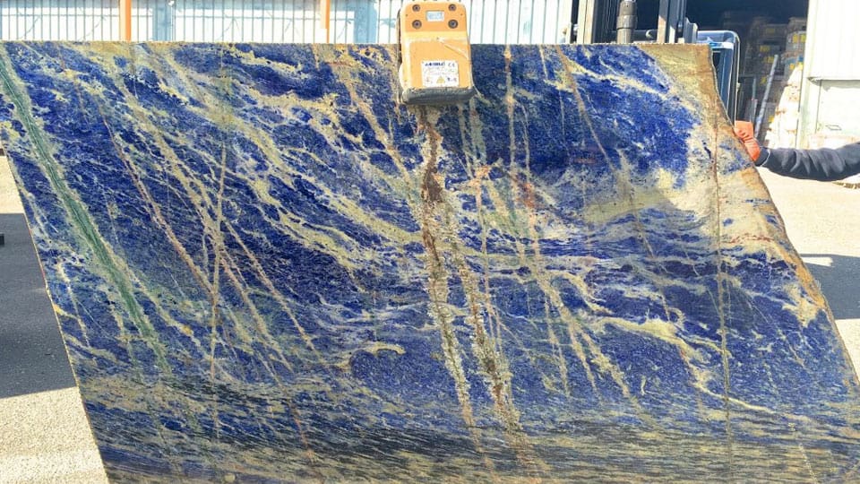 Tranche de sodalite bleue de Bolivie soulevée par une pince de manutention dans la cour de l'atelier