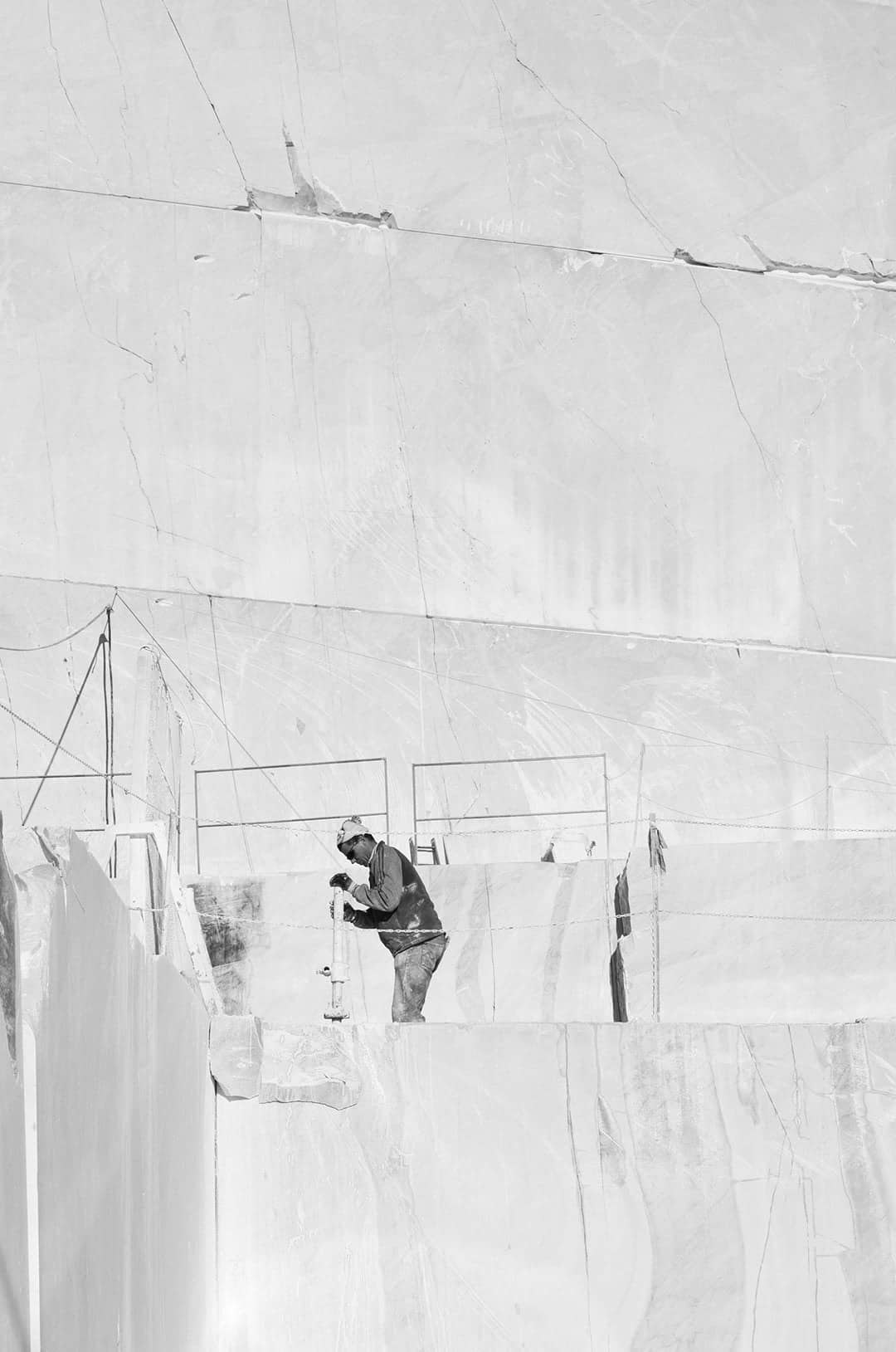 Carrière de marbre en noir et blanc, un carrier au travail sur un gradin de blocs sciés