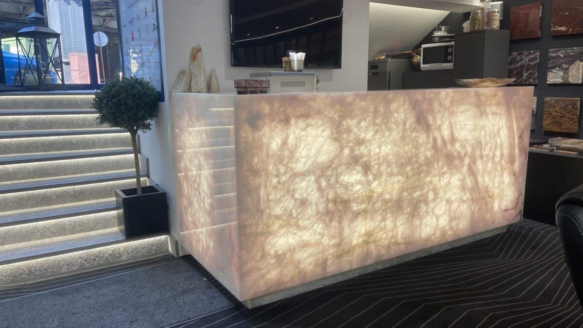 Banque d'accueil rétroéclairée en cristal rose dans un showroom, escalier et arbuste en pot à côté