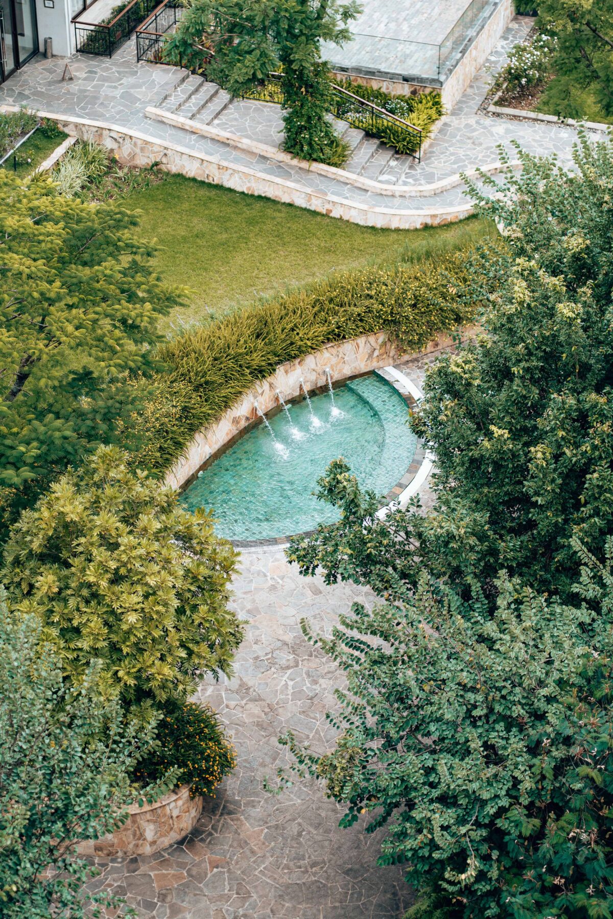 Piscine ovale entourée de dallage clair dans un jardin, vue aérienne