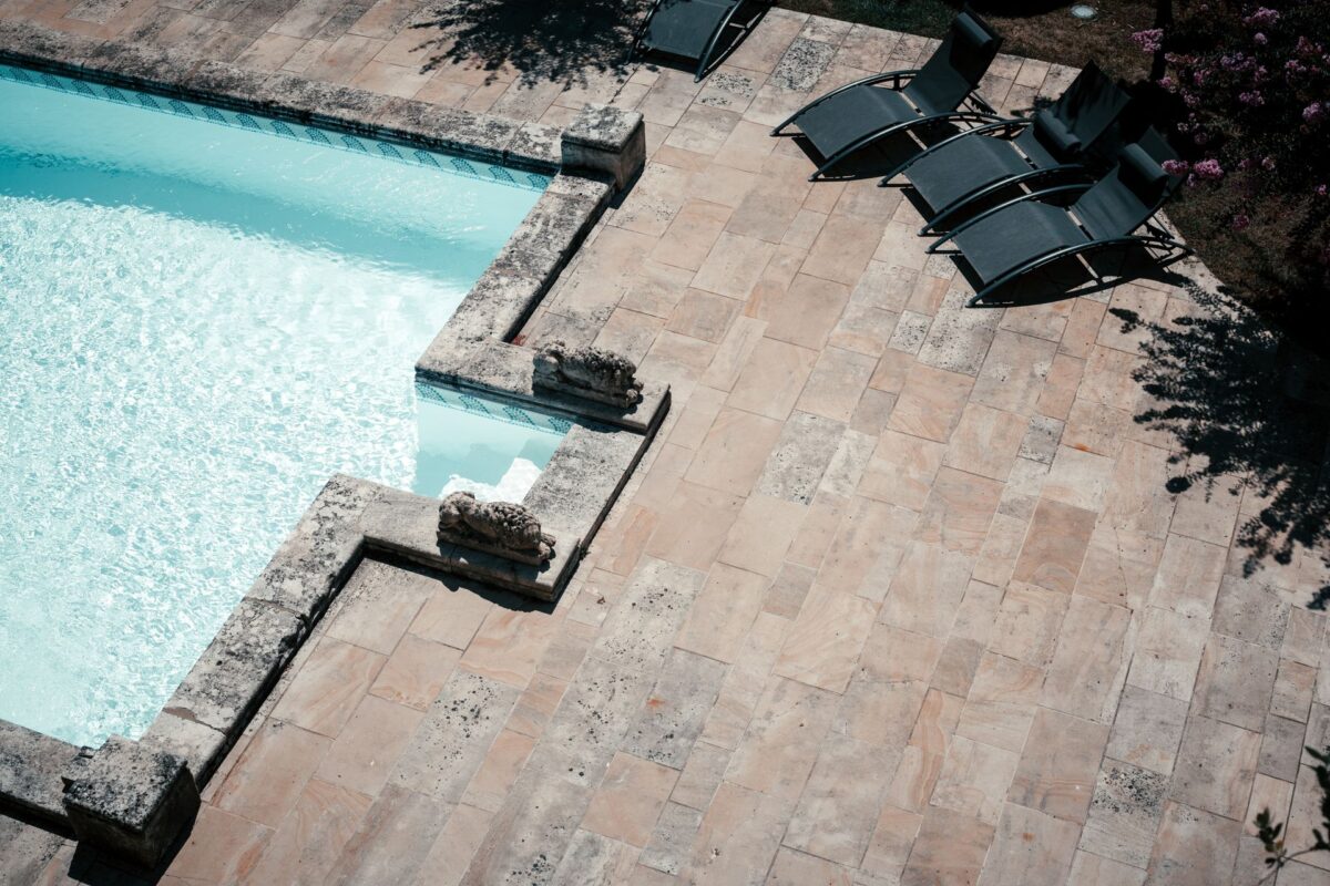 Terrasse de piscine en dalles de travertin vue du dessus avec transats